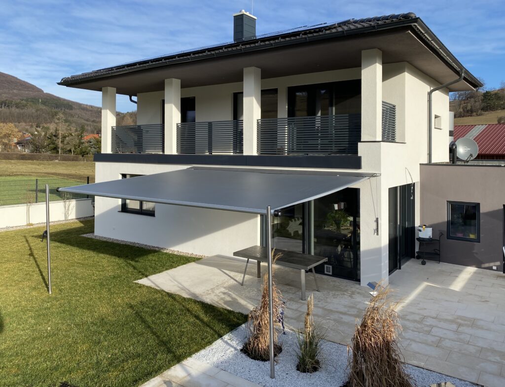 Modernes Einfamilienhaus mit großer, maßgefertigter Gelenkarmmarkise – effektiver Sonnenschutz für Terrasse von Rankl